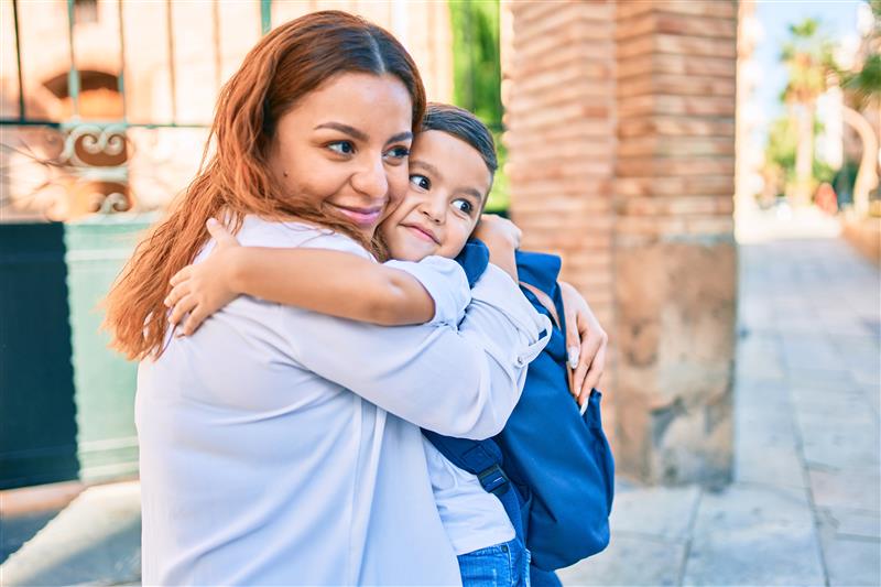 Mother hugging son with school backpack