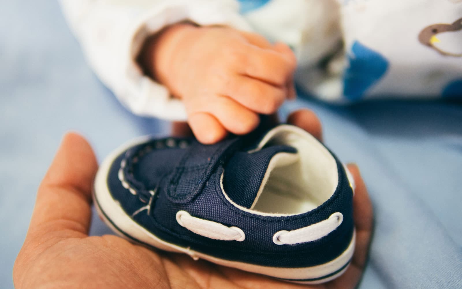 Baby holding tiny blue shoe on hand