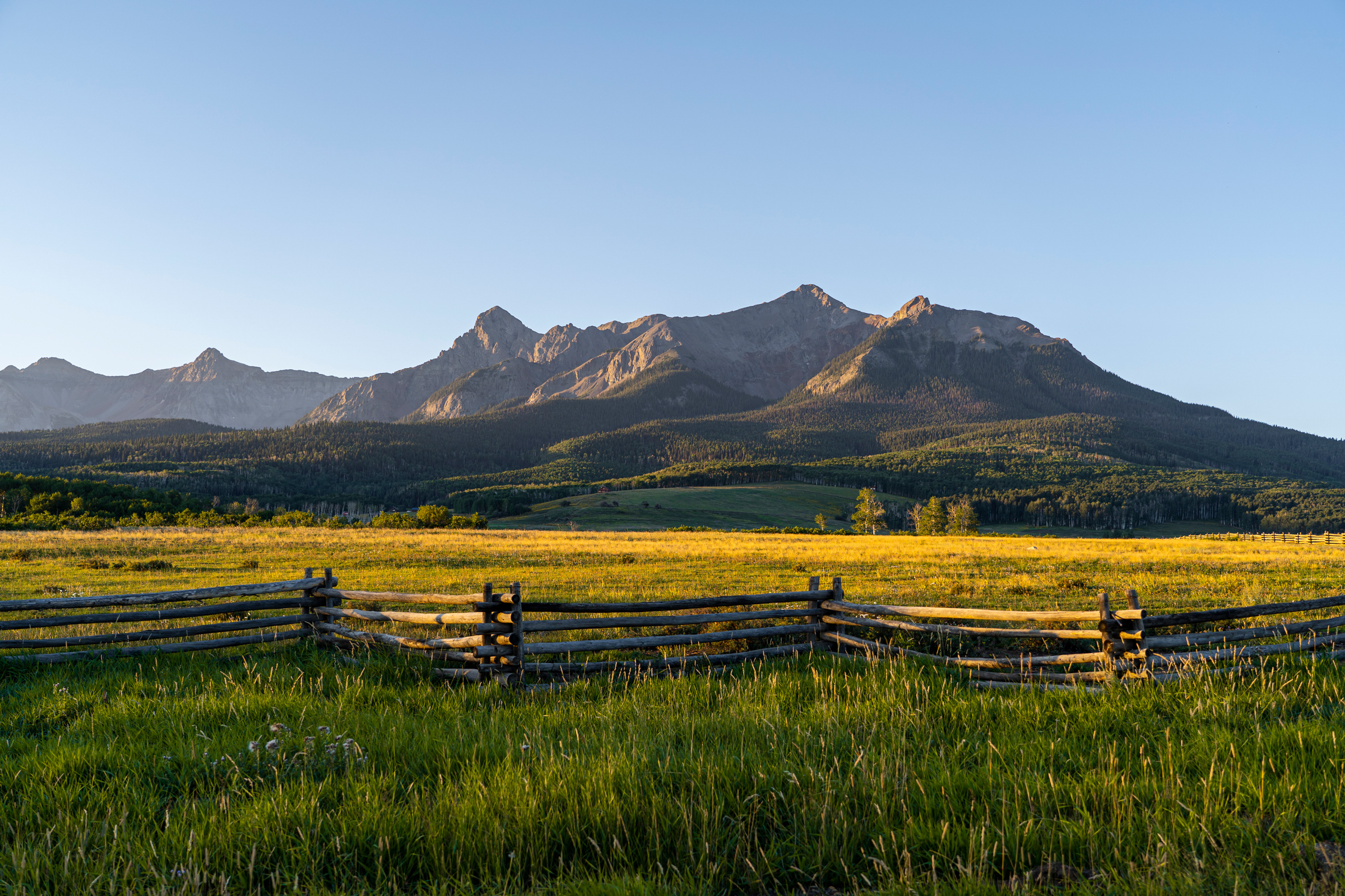 Mountain range behind sunny green meadow fence