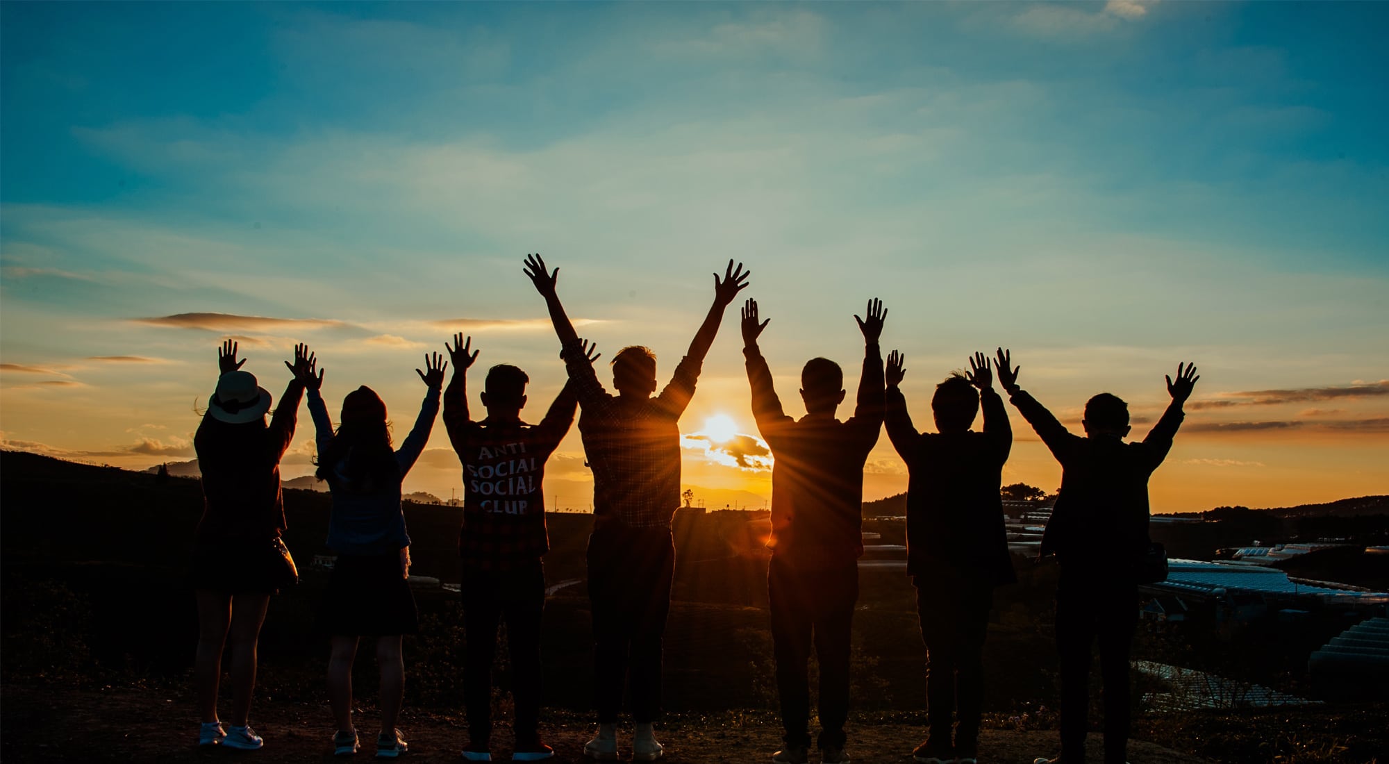 Group celebrating sunset with raised hands outdoors